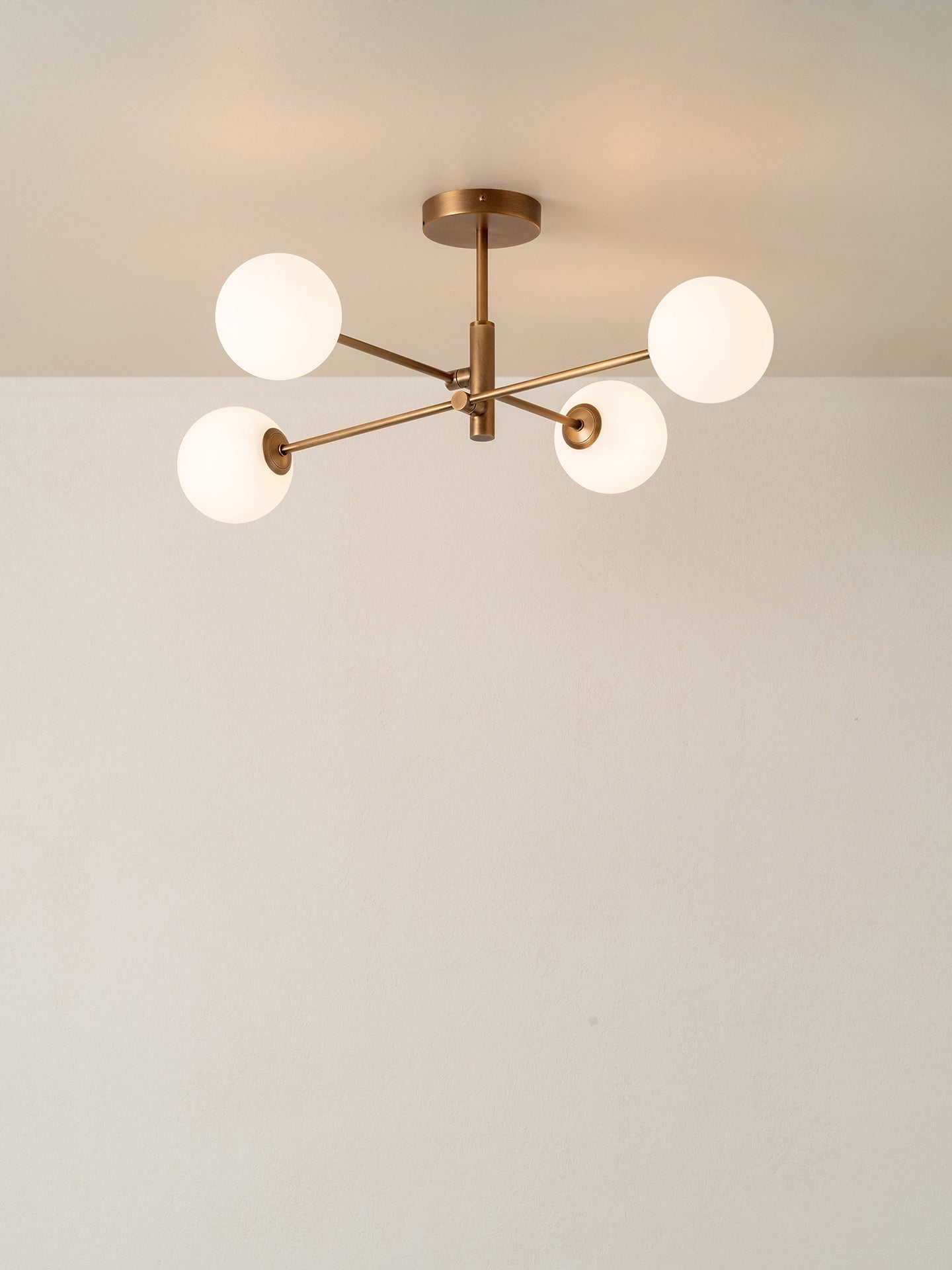 A modern four-light ceiling fixture with a bronze-finished metal frame and spherical frosted glass shades, shown installed on a ceiling against a plain off-white wall.