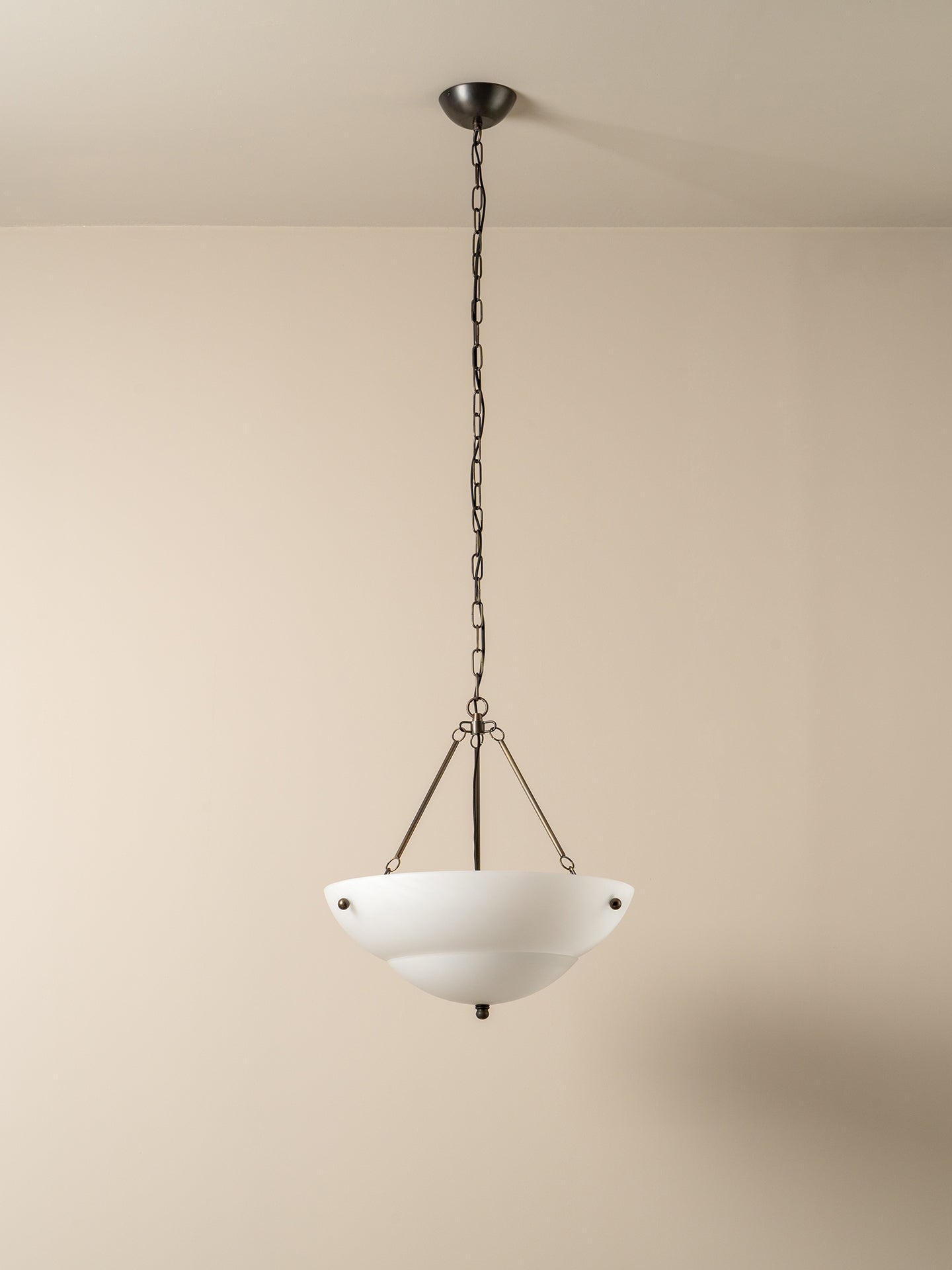 A modern pendant light with a white bowl-shaped glass shade and a dark metal chain and canopy, hanging against a plain beige wall.