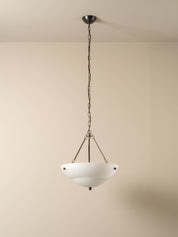 A modern pendant light with a white bowl-shaped glass shade and a dark metal chain and canopy, hanging against a plain beige wall.