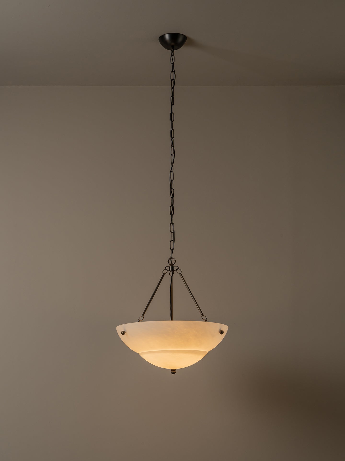 A hanging pendant light with a dark metal chain and frame, featuring a warm white frosted glass bowl shade, shown against a plain beige wall and ceiling.