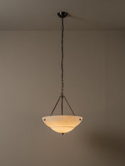 A hanging pendant light with a dark metal chain and frame, featuring a warm white frosted glass bowl shade, shown against a plain beige wall and ceiling.