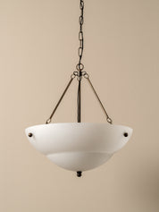 A modern pendant light fixture with a wide, bowl-shaped white frosted glass shade suspended by a dark metal chain and three angled rods against a solid beige background.