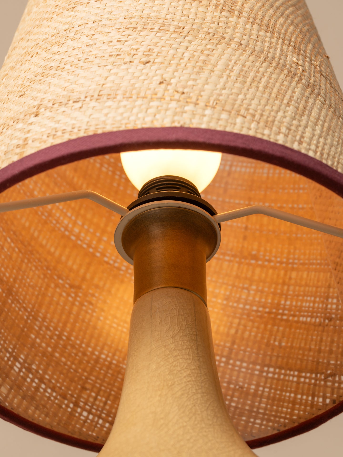 Close-up of a woven natural fiber table lamp shade with a warm glowing bulb inside and a dark purple inner rim.