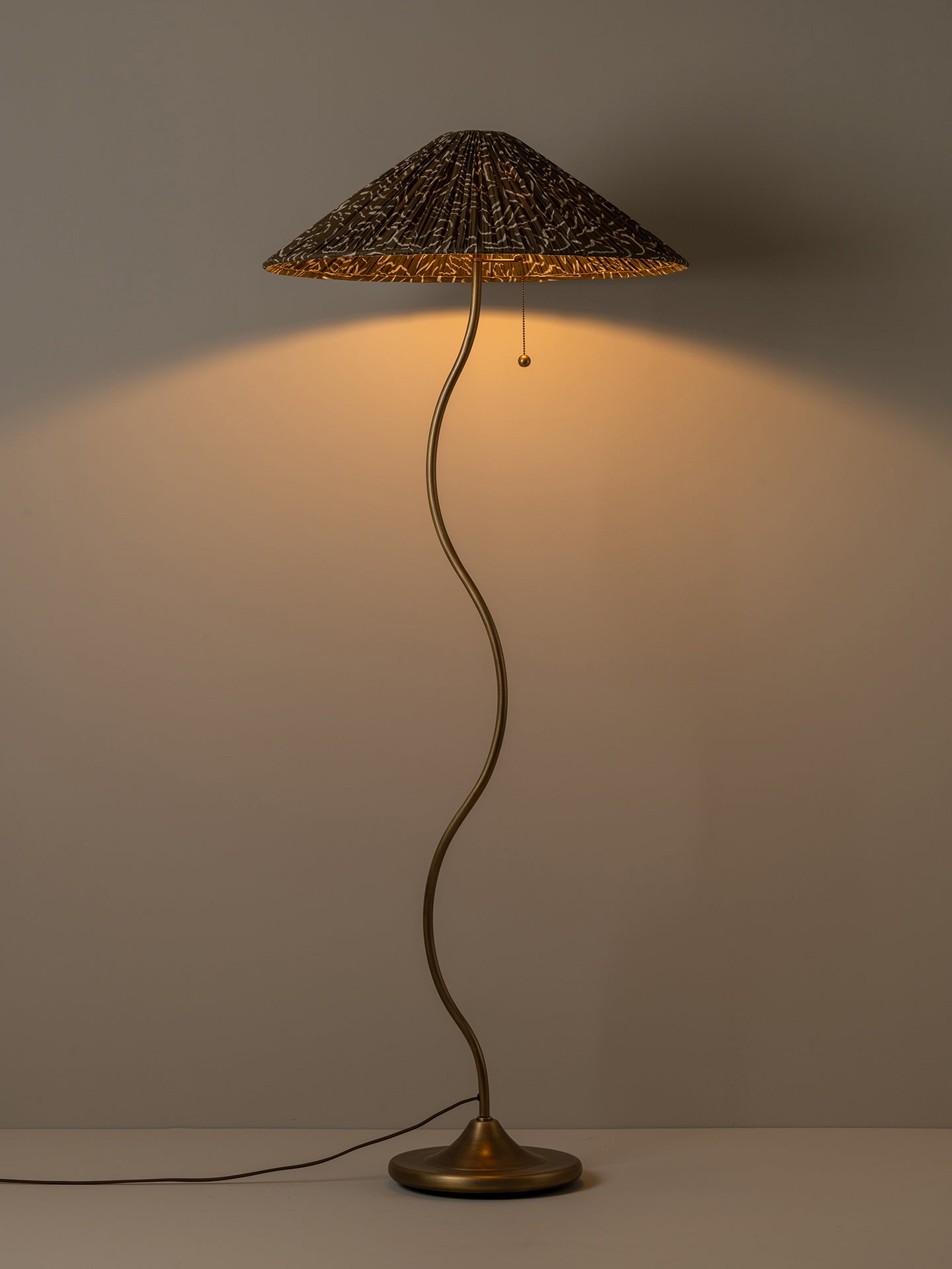 A mushroom-shaped table lamp with a textured brown and gold patterned conical shade, a curved metallic stem, and a round base, shown lit against a neutral background.