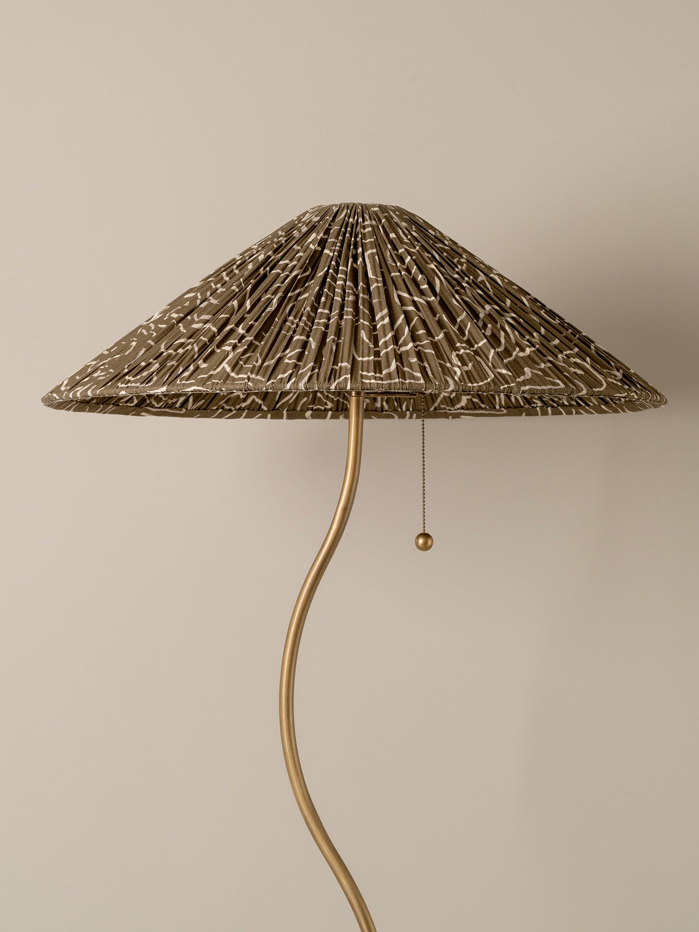 A floor lamp with a pleated conical shade in a brown and beige abstract pattern, supported by a curved gold metal stem with a pull chain.