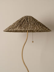 A floor lamp with a pleated conical shade in a brown and beige abstract pattern, supported by a curved gold metal stem with a pull chain.