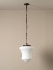 A modern pendant light with a white bell-shaped glass shade and a dark bronze metal canopy and chain, shown hanging against a neutral beige wall.