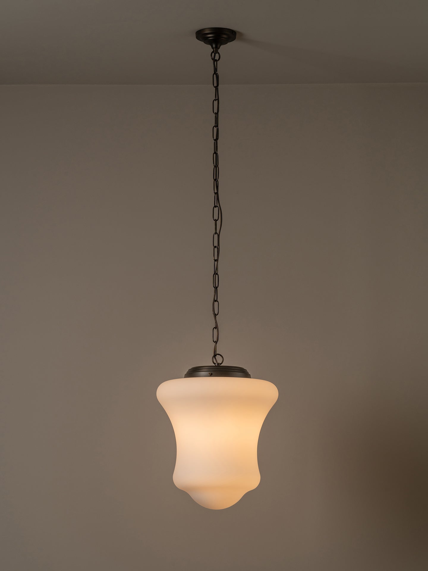 A hanging pendant light with a warm white frosted glass shade and a dark metal chain and canopy, shown against a plain beige wall.