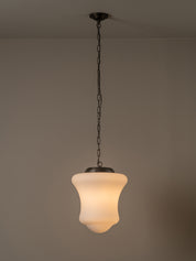 A hanging pendant light with a warm white frosted glass shade and a dark metal chain and canopy, shown against a plain beige wall.