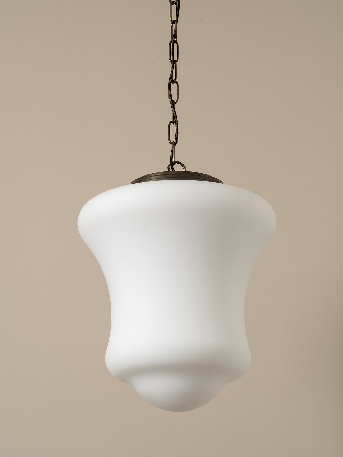 A modern pendant light with a white, bell-shaped frosted glass shade and a dark metal chain, shown against a solid beige background.