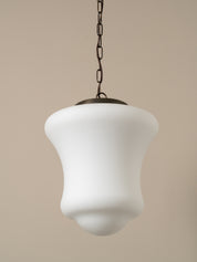 A modern pendant light with a white, bell-shaped frosted glass shade and a dark metal chain, shown against a solid beige background.