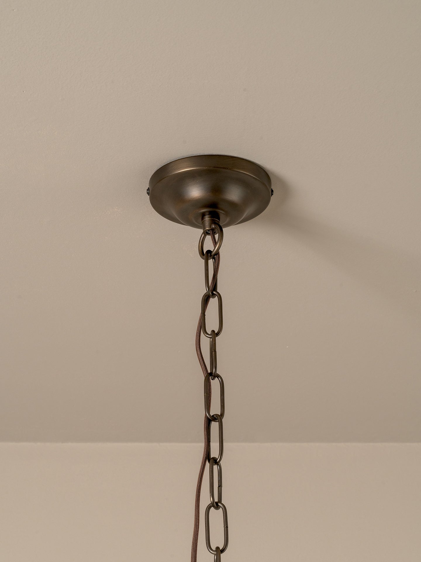 An industrial-style ceiling light fixture with a round, dark bronze ceiling canopy and a matching metal hanging chain, shown against a plain beige wall and ceiling.