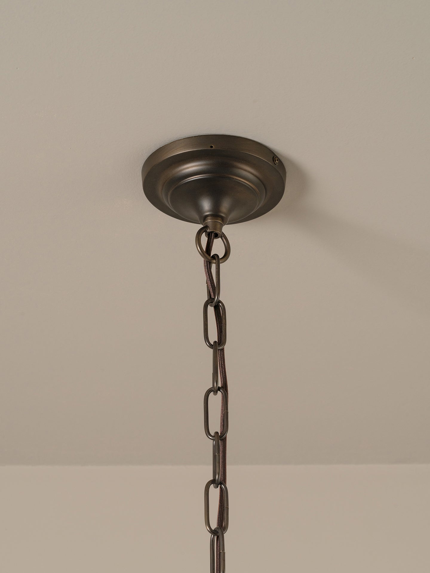  a dark bronze metal canopy and chain, shown hanging against a neutral beige wall.