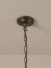  a dark bronze metal canopy and chain, shown hanging against a neutral beige wall.