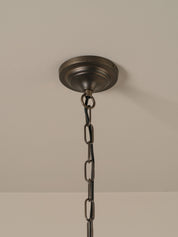  a dark bronze metal canopy and chain, shown hanging against a neutral beige wall.