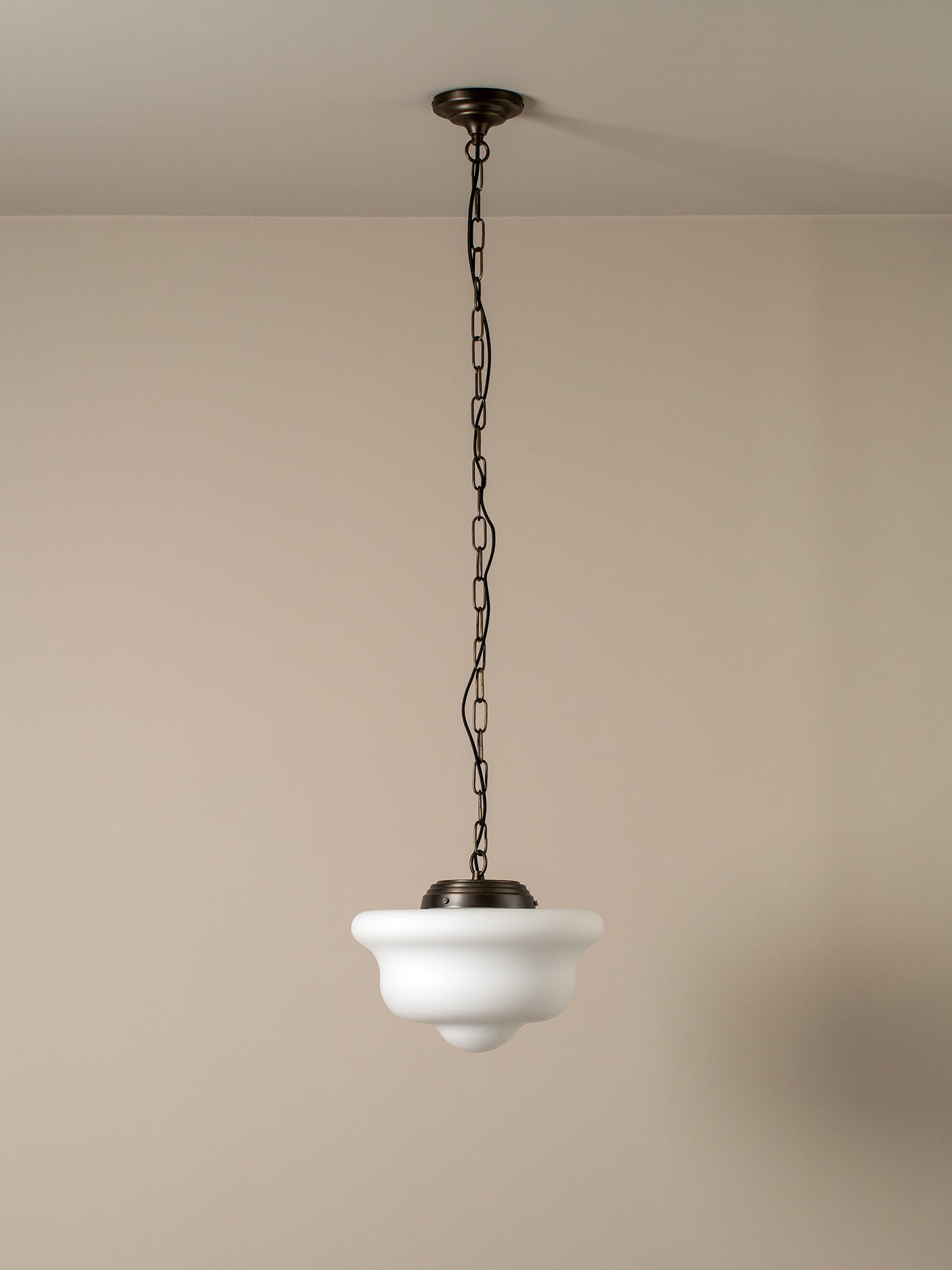 A hanging pendant light with a white bowl-shaped glass shade and a dark metal chain and canopy, shown against a plain beige wall and ceiling.
