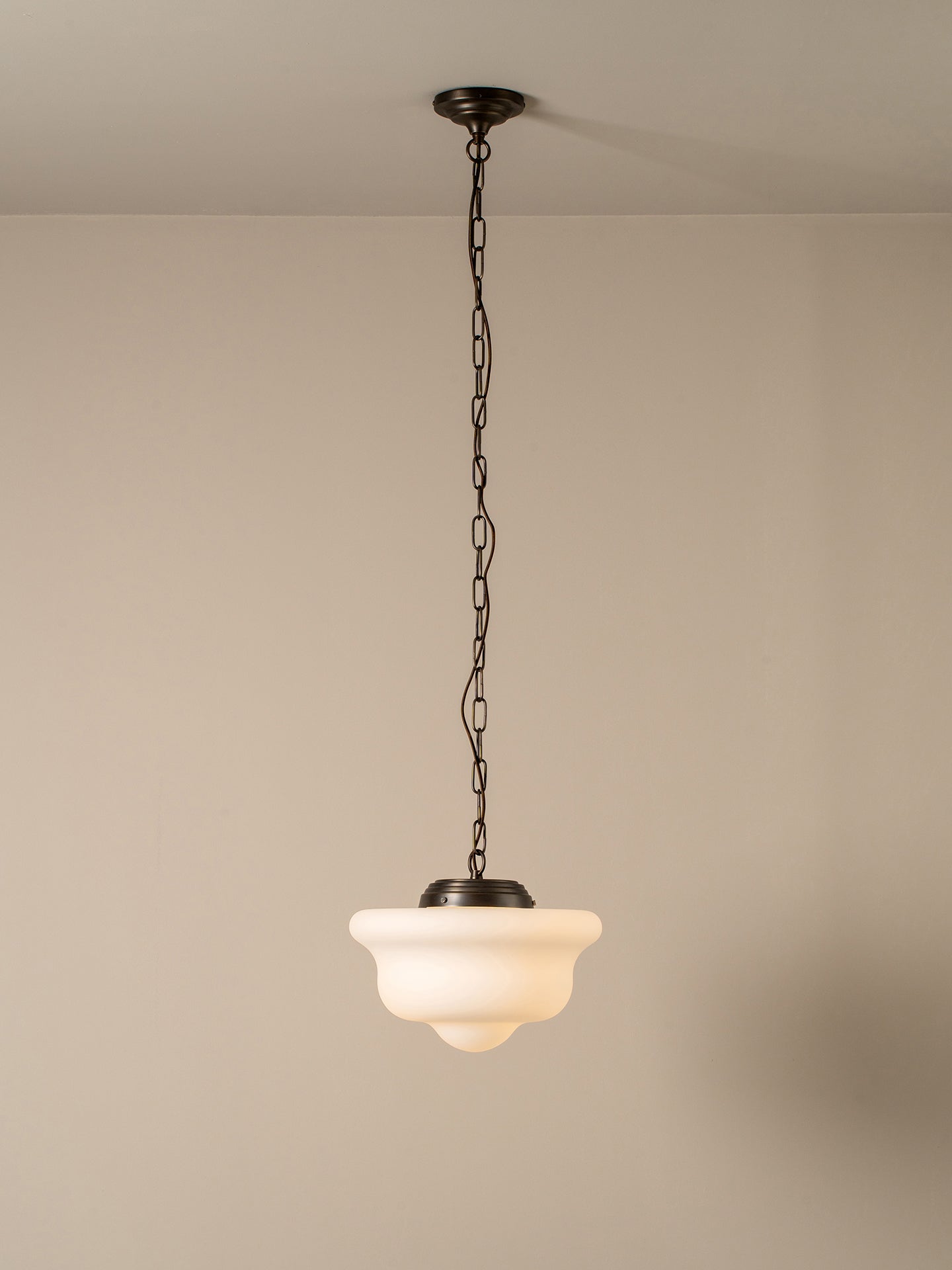 A single pendant light with a dark metal chain and canopy, featuring a warm white frosted glass shade, shown hanging against a plain beige wall and ceiling.