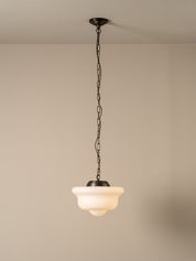 A single pendant light with a dark metal chain and canopy, featuring a warm white frosted glass shade, shown hanging against a plain beige wall and ceiling.