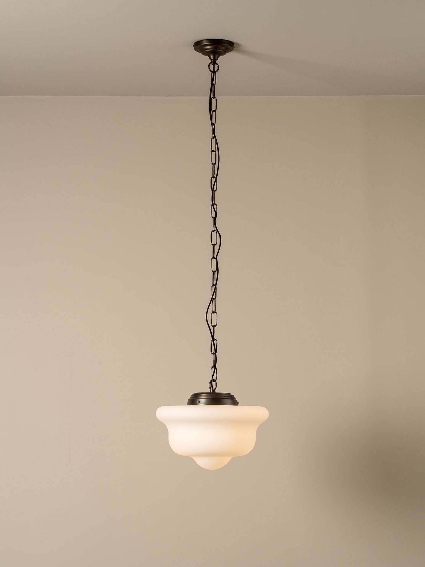 A single pendant light with a dark metal chain and canopy, featuring a warm white frosted glass shade, shown hanging against a neutral beige wall and ceiling.