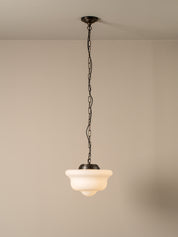 A single pendant light with a dark metal chain and canopy, featuring a warm white frosted glass shade, shown hanging against a neutral beige wall and ceiling.