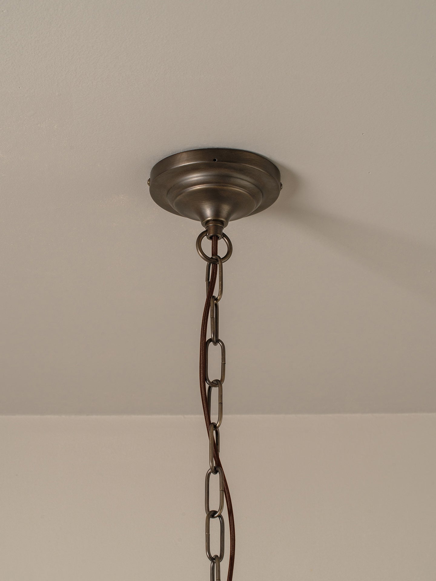 An antique bronze ceiling light fixture canopy hanging from a black metal chain against a neutral off-white wall and ceiling.