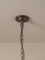 An antique bronze ceiling light fixture canopy hanging from a black metal chain against a neutral off-white wall and ceiling.