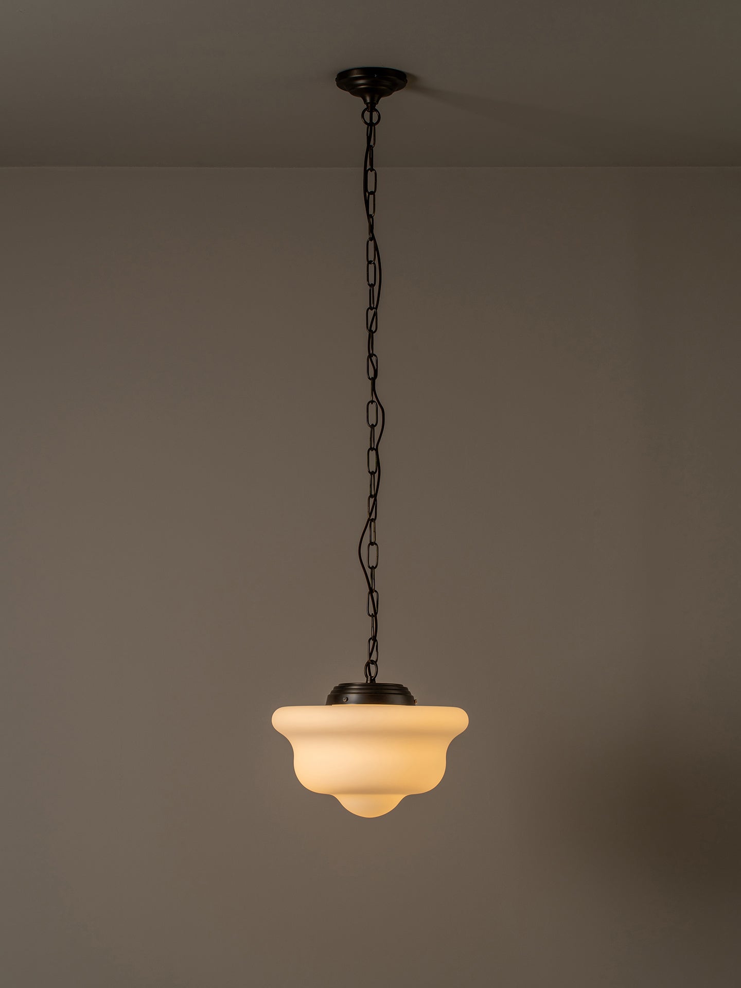 A hanging pendant light with a frosted warm-white glass shade and dark metal chain and canopy, shown against a plain taupe wall and ceiling.