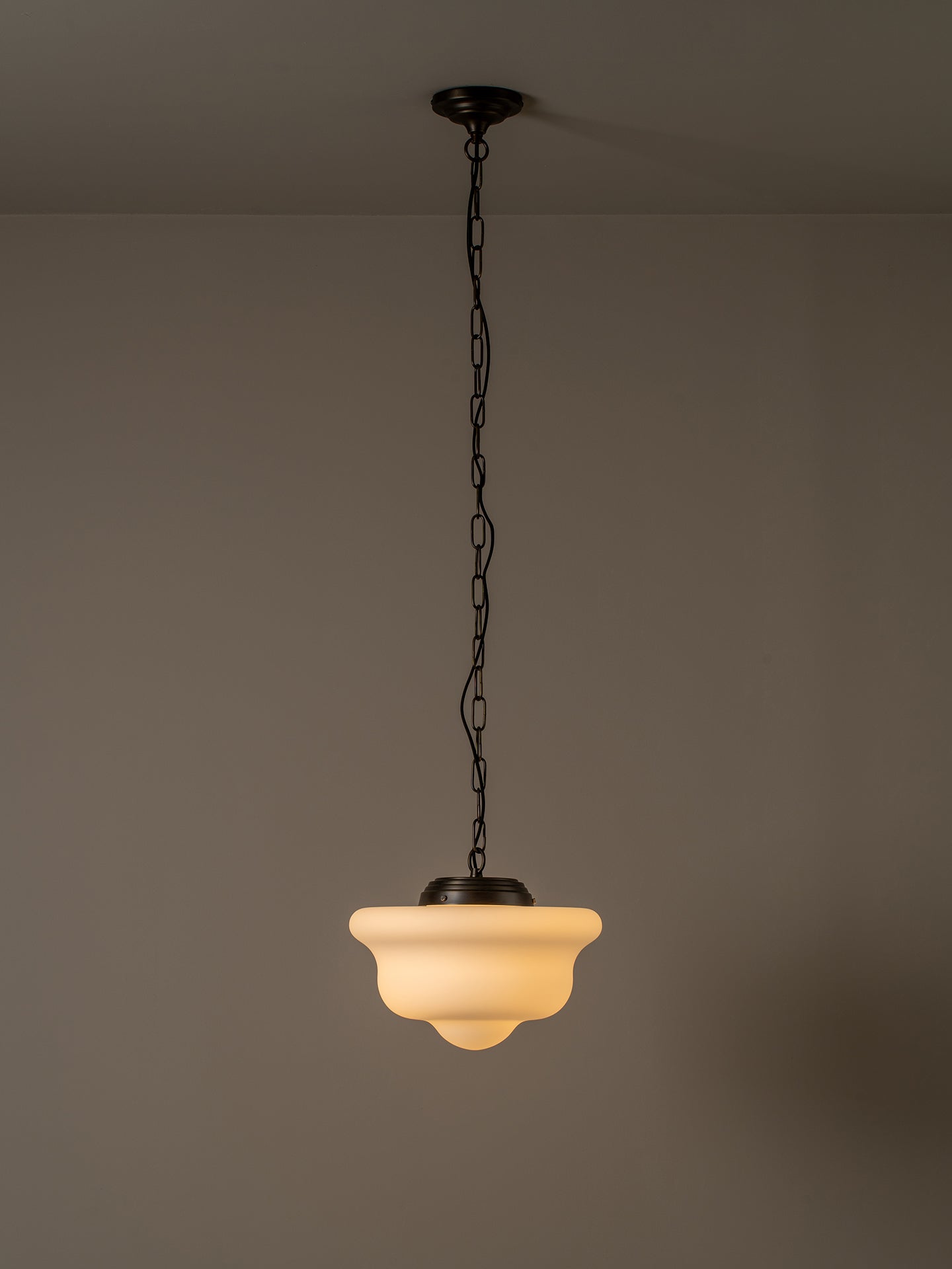 A vintage-style pendant light with a warm white frosted glass shade and a dark metal chain and ceiling mount, shown hanging against a plain gray wall.