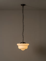 A vintage-style pendant light with a warm white frosted glass shade and a dark metal chain and ceiling mount, shown hanging against a plain gray wall.