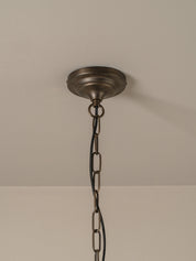 An antique bronze ceiling light fixture canopy hanging from a black metal chain against a neutral off-white wall and ceiling.