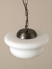A modern pendant light with a wide, tiered white glass shade and a dark bronze metal canopy and chain, shown against a solid beige background.