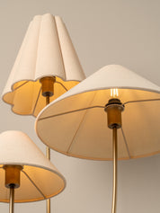 Three modern table lamps with pleated beige fabric shades and warm brass metal stems, shown against a neutral light gray background.