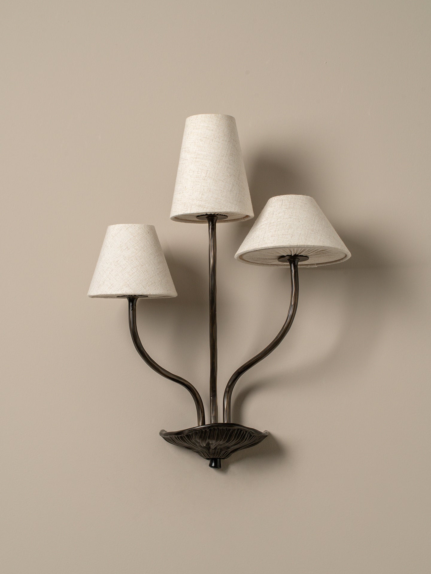 Three-light wall sconce with white lampshades on a beige wall