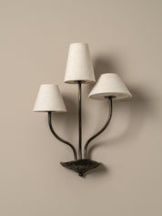 Three-light wall sconce with white lampshades on a beige wall