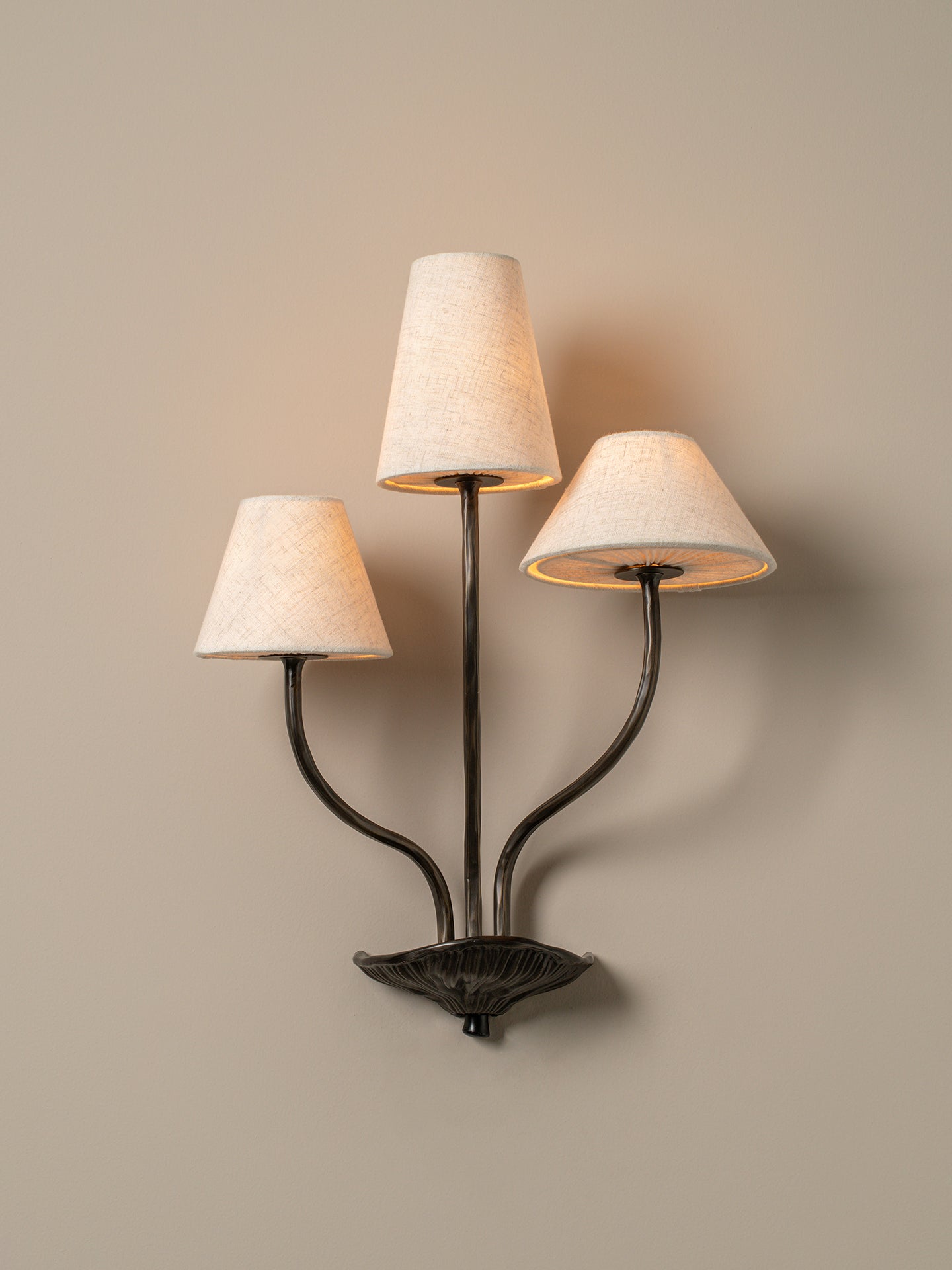 Three-light wall sconce with lampshades on a beige wall
