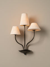 Three-light wall sconce with lampshades on a beige wall