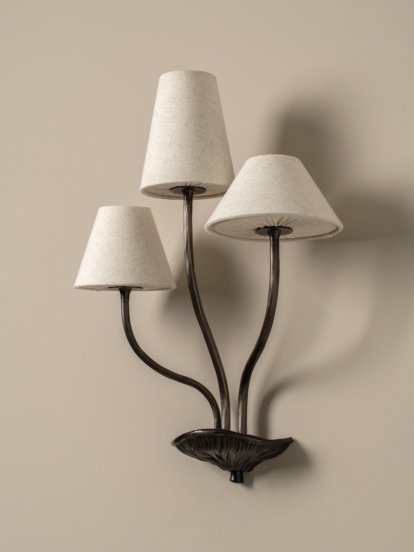 Wall-mounted lamp with three lampshades on a beige wall