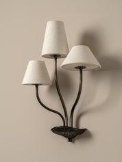 Wall-mounted lamp with three lampshades on a beige wall