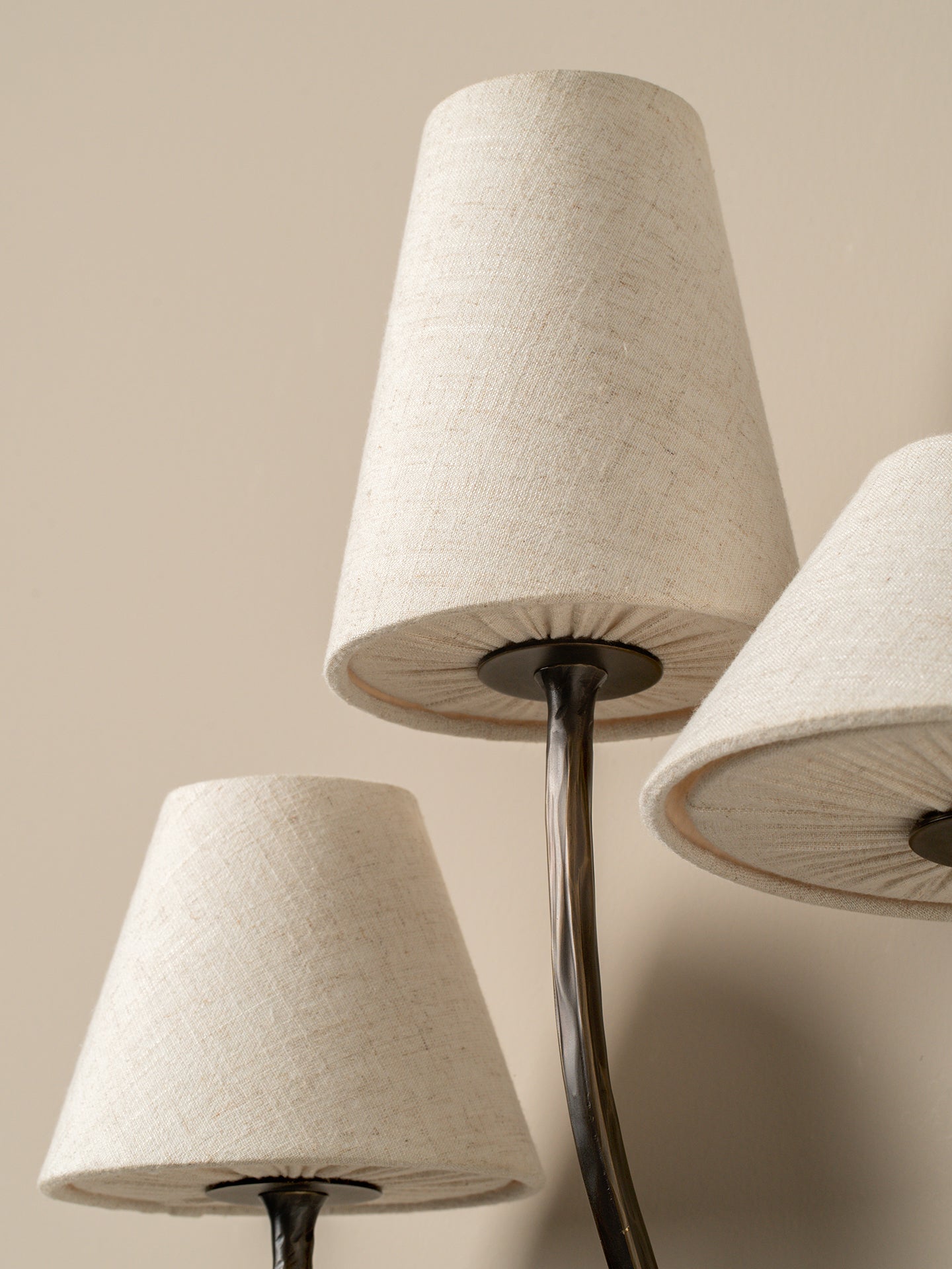 Close-up of a lamp with three beige lampshades on a neutral background