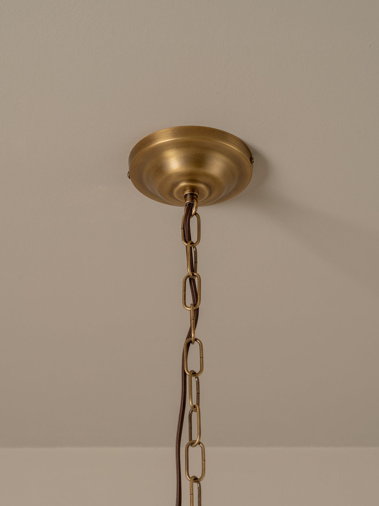 A brass ceiling canopy and hanging chain for a light fixture, shown mounted on a beige wall.