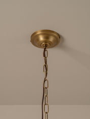 A brass ceiling canopy and hanging chain for a light fixture, shown mounted on a beige wall.