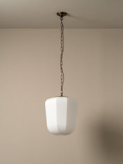 A modern pendant light with a frosted white cylindrical shade and a dark metal chain hanging from a ceiling, shown against a plain beige wall.