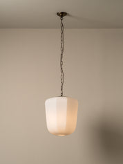 A modern pendant light with a frosted white cylindrical shade and a dark metal chain hanging from a ceiling, shown against a plain beige wall.