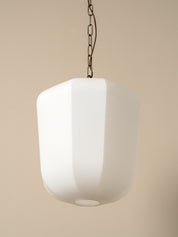 A modern white pendant light with a faceted, rounded cylindrical shade hanging from a dark metal chain against a solid beige background.