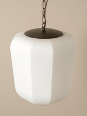 A modern pendant light with a matte white faceted glass shade and a dark bronze metal top cap and chain, shown against a solid beige background.