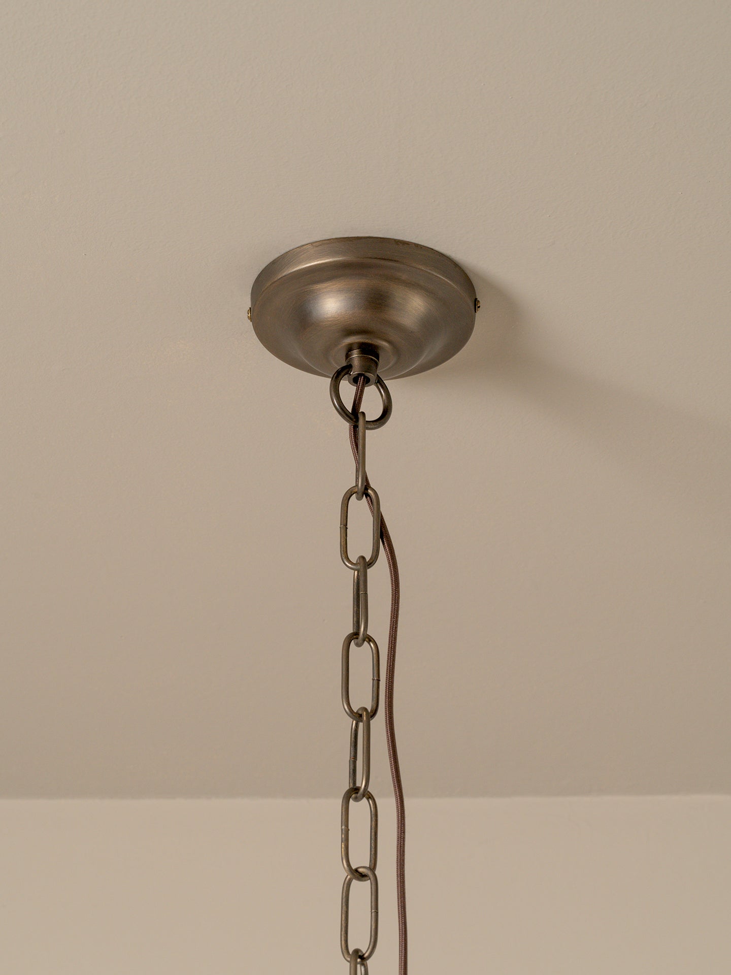 An industrial-style ceiling light fixture canopy with a hanging chain, shown against a plain beige wall and ceiling.
