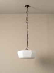 A modern pendant light with a white faceted glass shade suspended by a dark metal chain from a ceiling canopy, set against a minimalist beige wall.