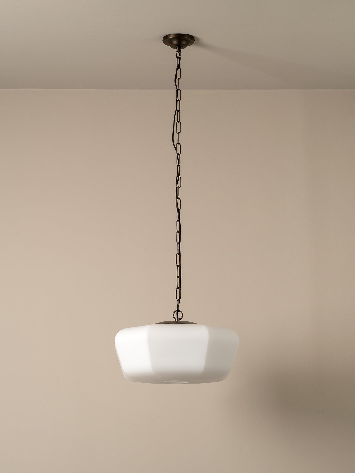 A modern pendant light with a white faceted glass shade suspended by a dark metal chain from a matching ceiling canopy, set against a plain beige wall.