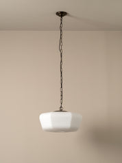 A modern pendant light with a white faceted glass shade suspended by a dark metal chain from a matching ceiling canopy, set against a plain beige wall.