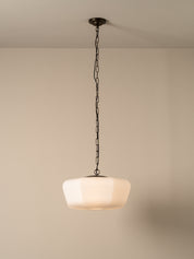 A modern pendant light with a frosted white glass shade and a dark metal chain hanging from the ceiling against a warm beige wall.